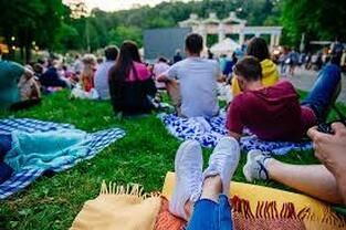 A group of people are sitting on blankets in the grass watching a movie.