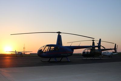 Two helicopters are parked on a runway at sunset.