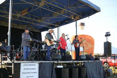 A group of men are playing instruments on a stage in front of a large bottle of whiskey.