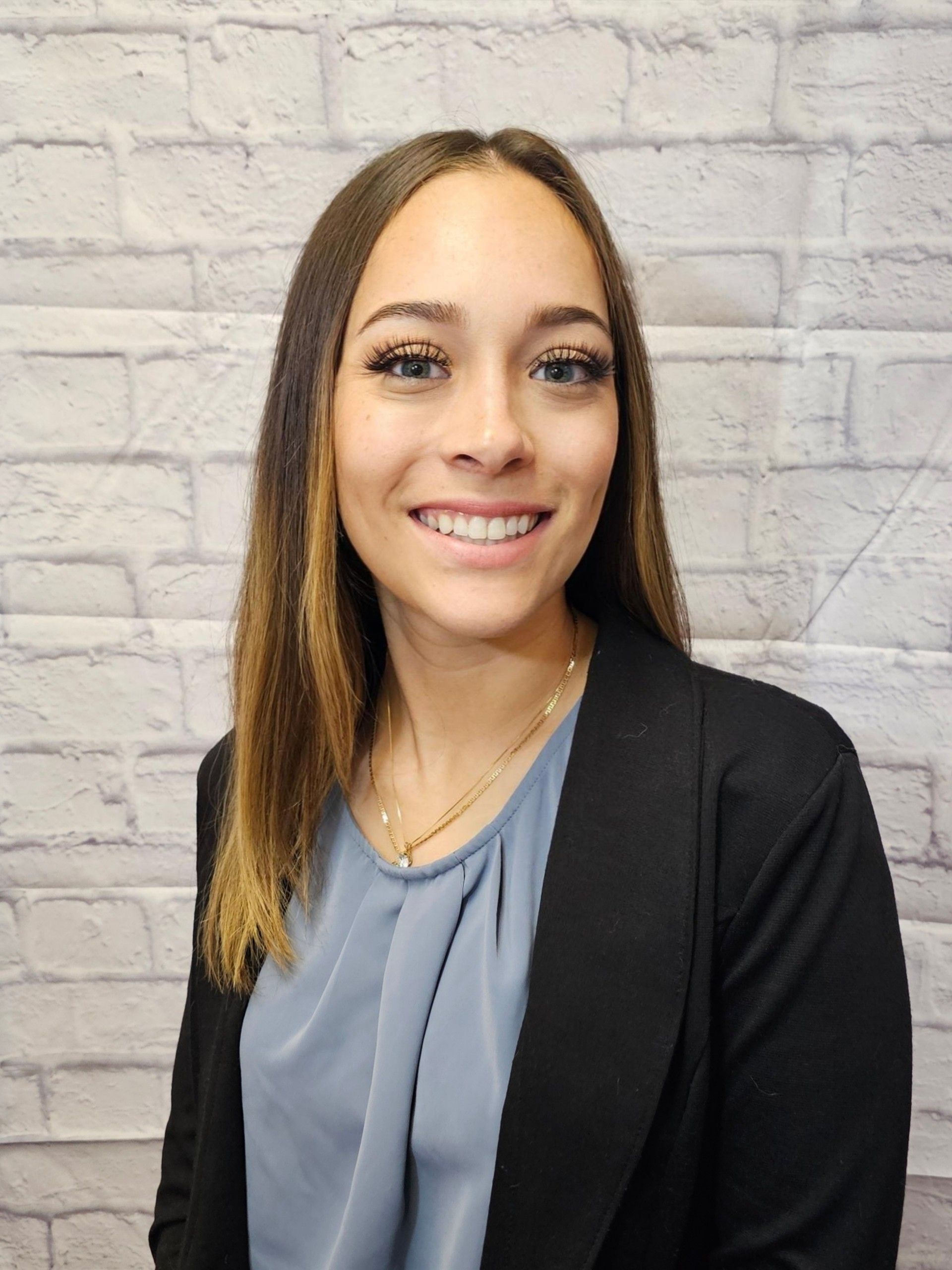 A woman in a suit and necklace is smiling for a picture.