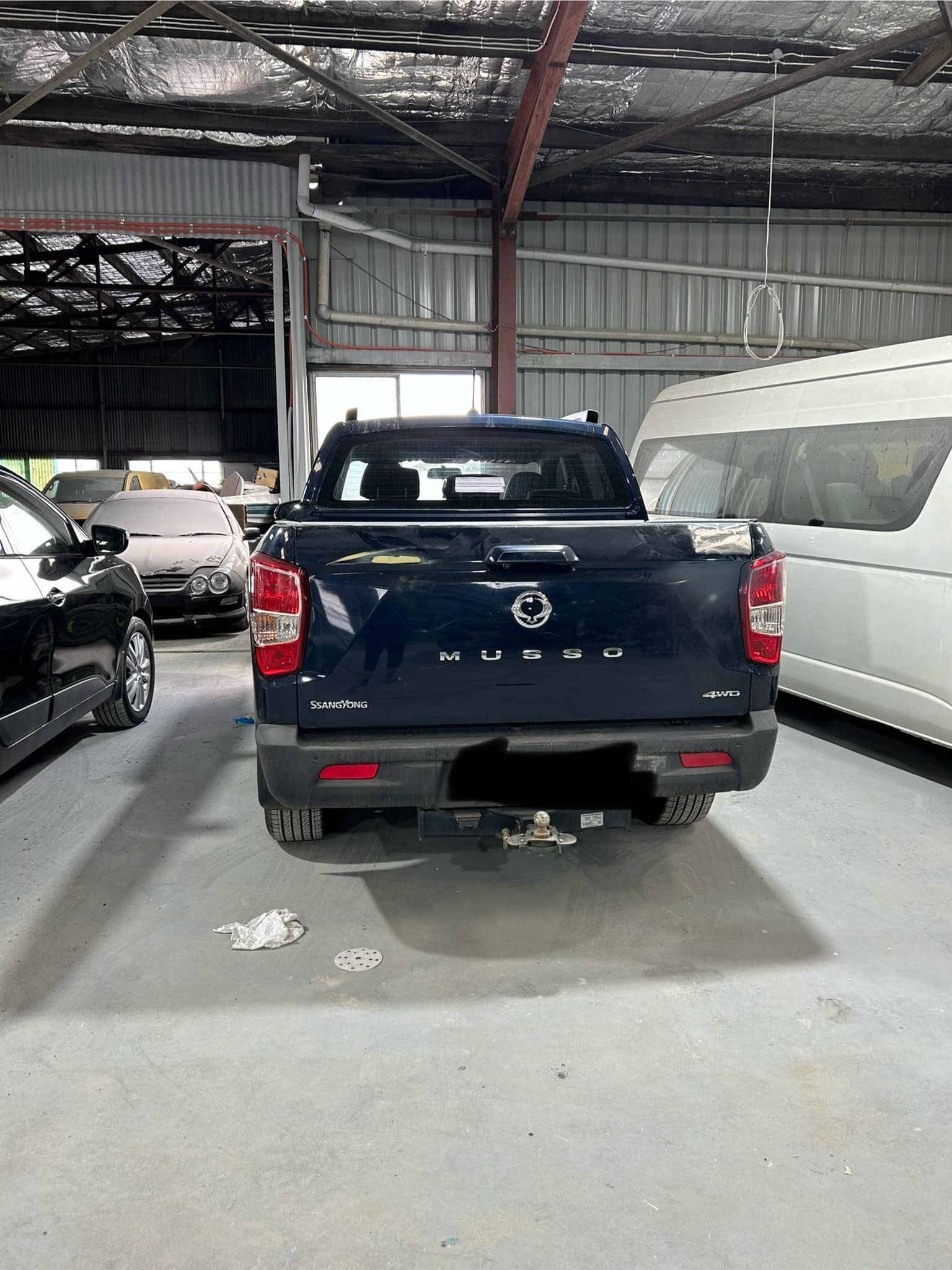 A blue truck is parked in a garage next to other cars.