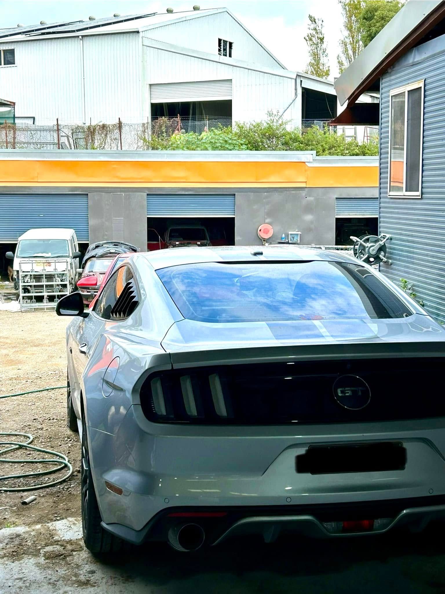 A silver mustang is parked in front of a garage.