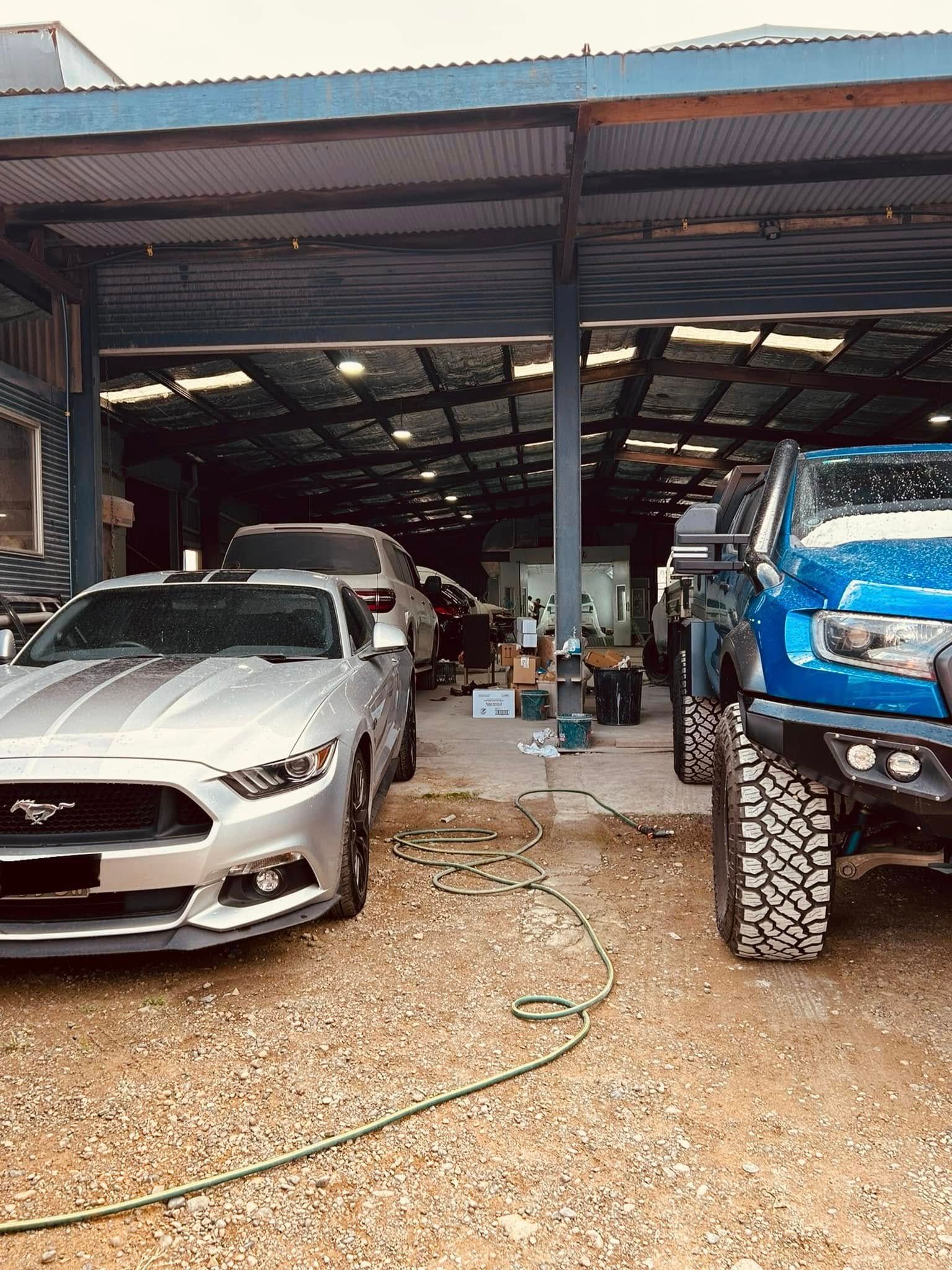 A silver mustang and a blue truck are parked in front of a garage.