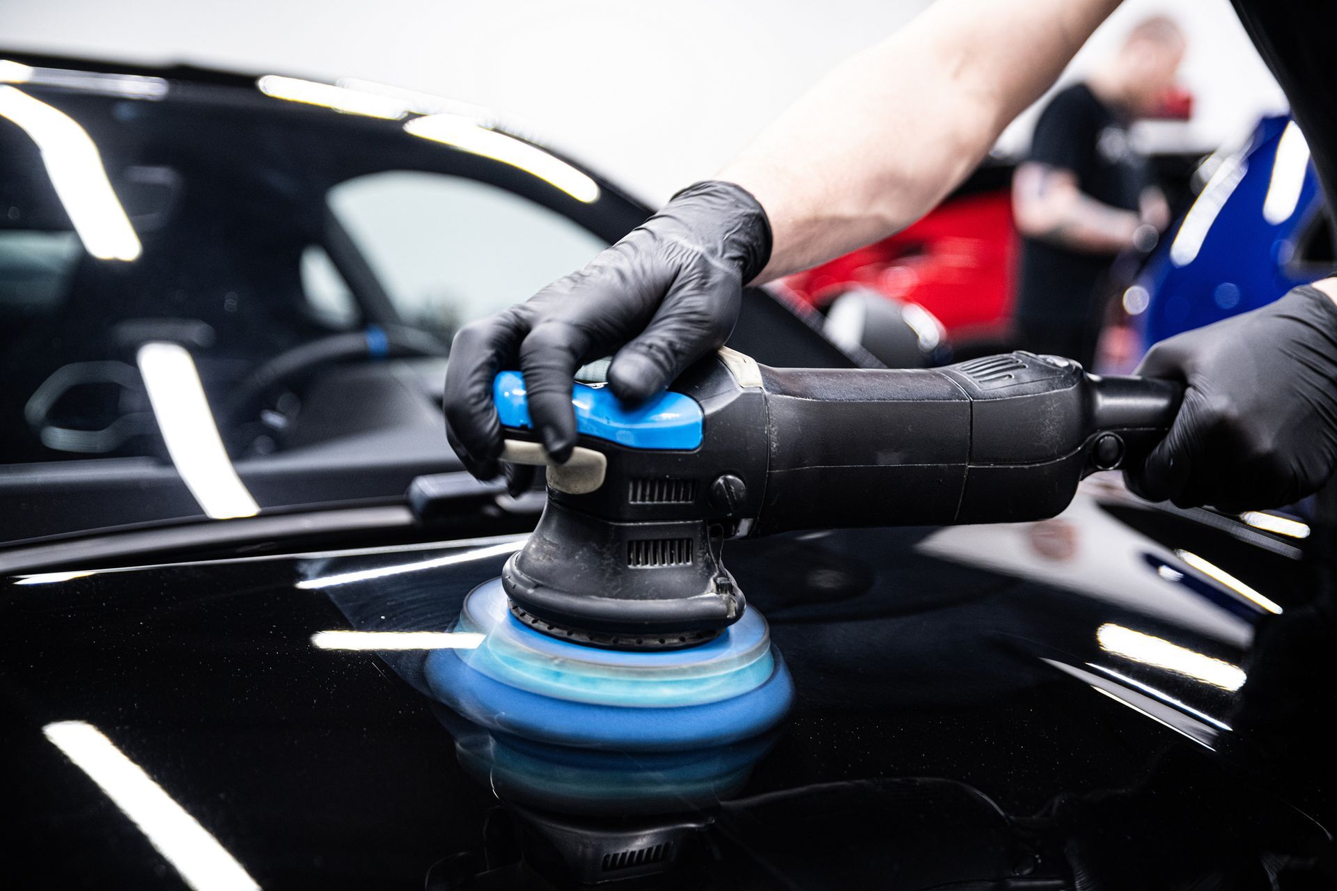 A person is polishing a black car with a machine.