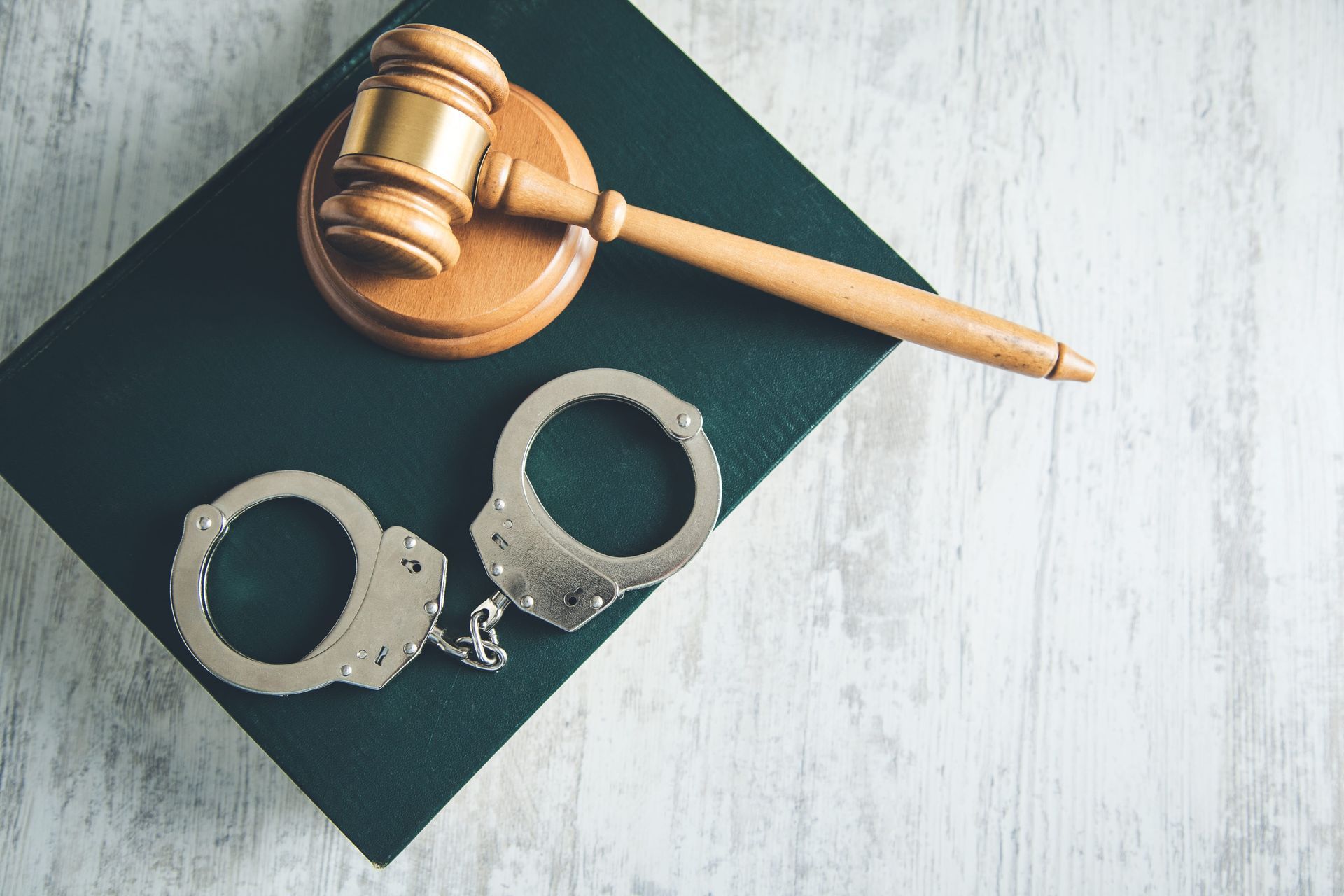 Handcuffs and a judgeās gavel on a dark folder over a light tabletop