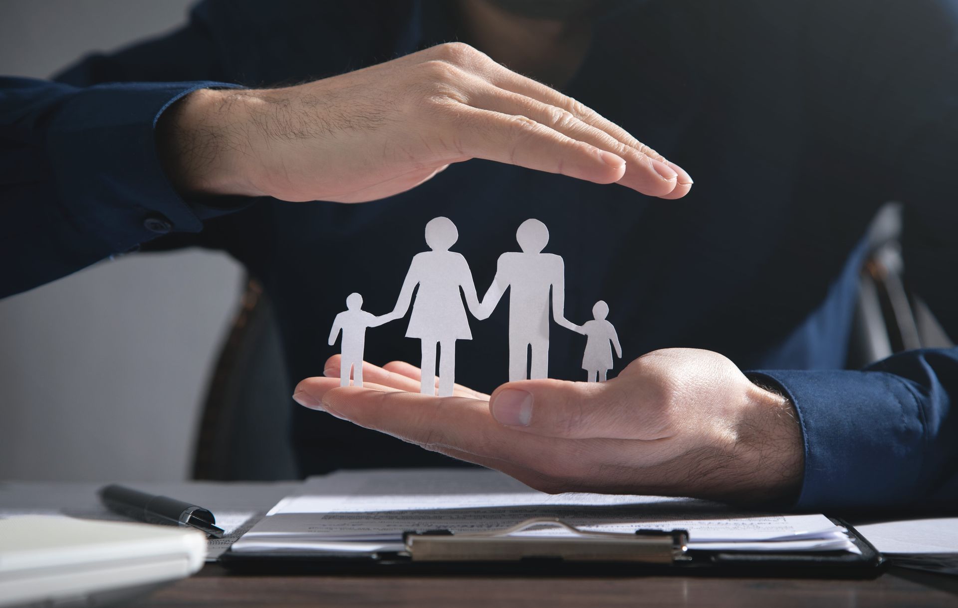 Hands protecting paper cutout family figures on a desk in an office setting