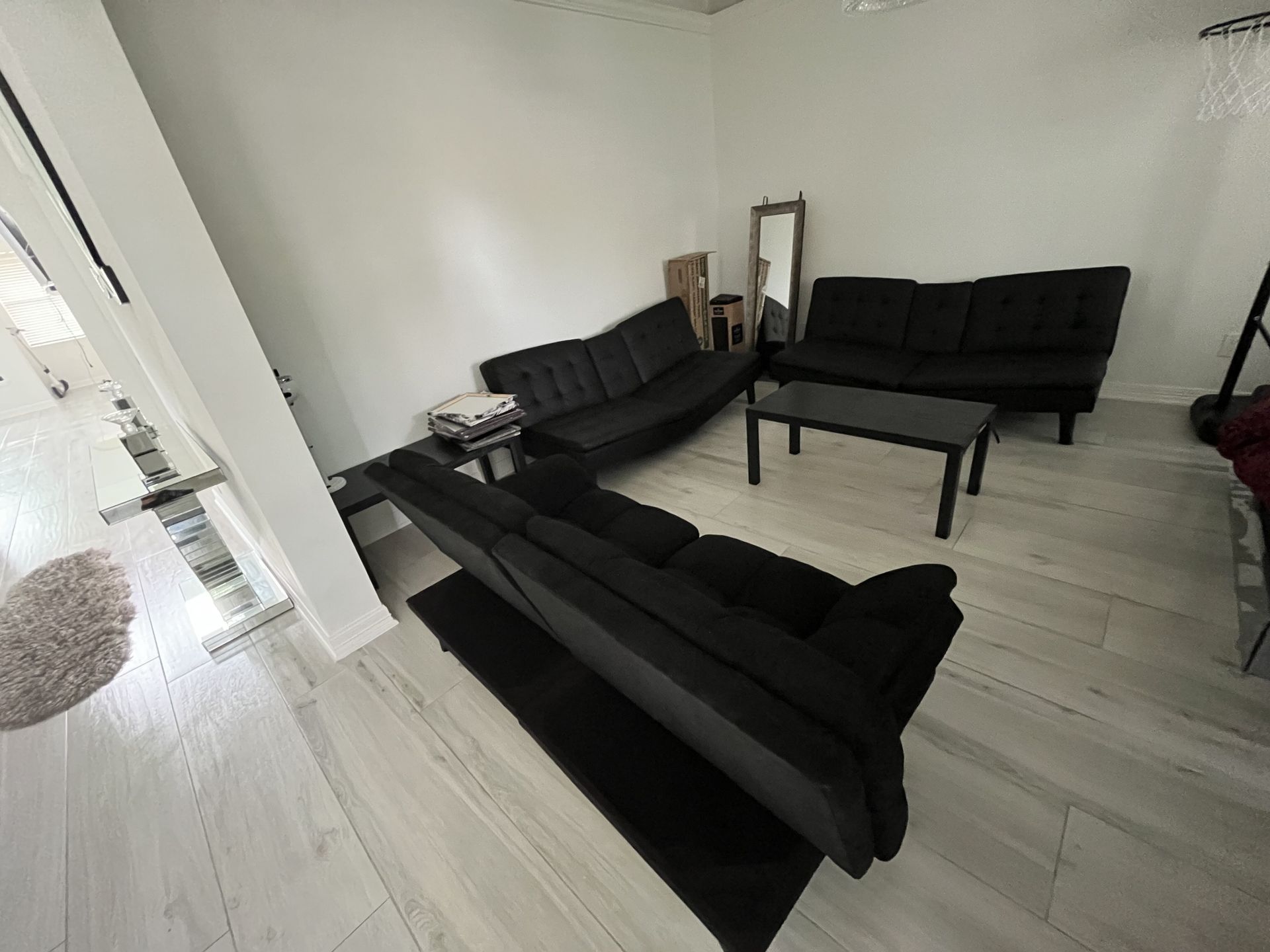 A living room with black couches , a coffee table , and a mirror.