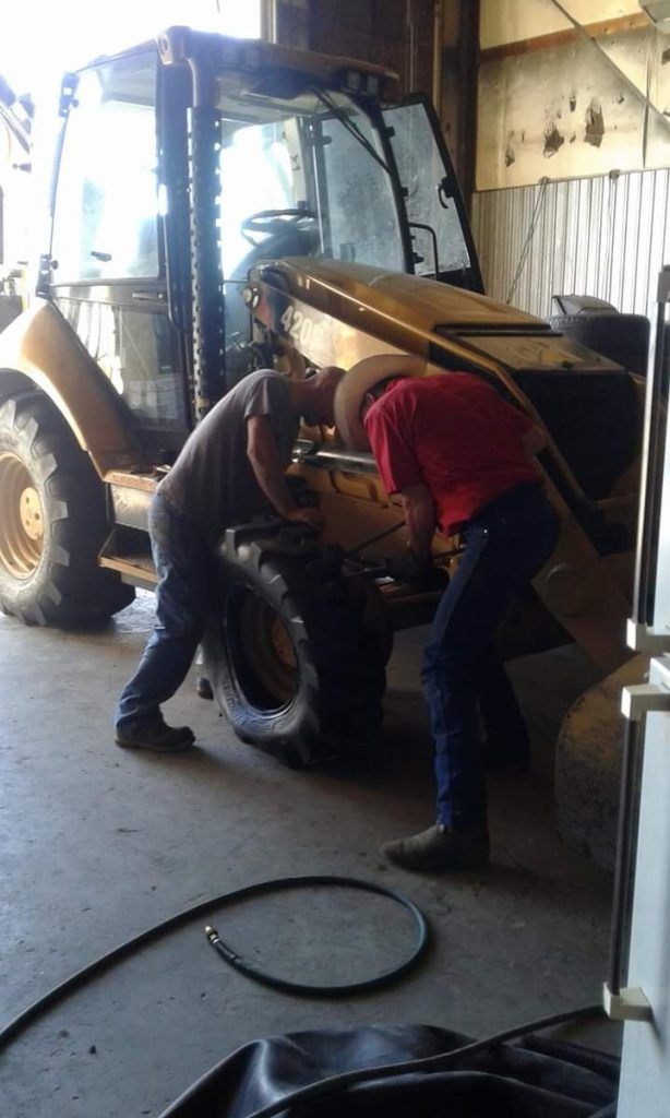 Two people working on a yellow construction vehicle inside a garage.