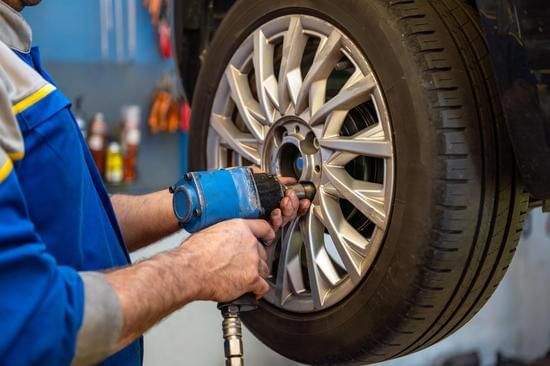 Red car on a white tow truck, parked on a road with green trees in the background.