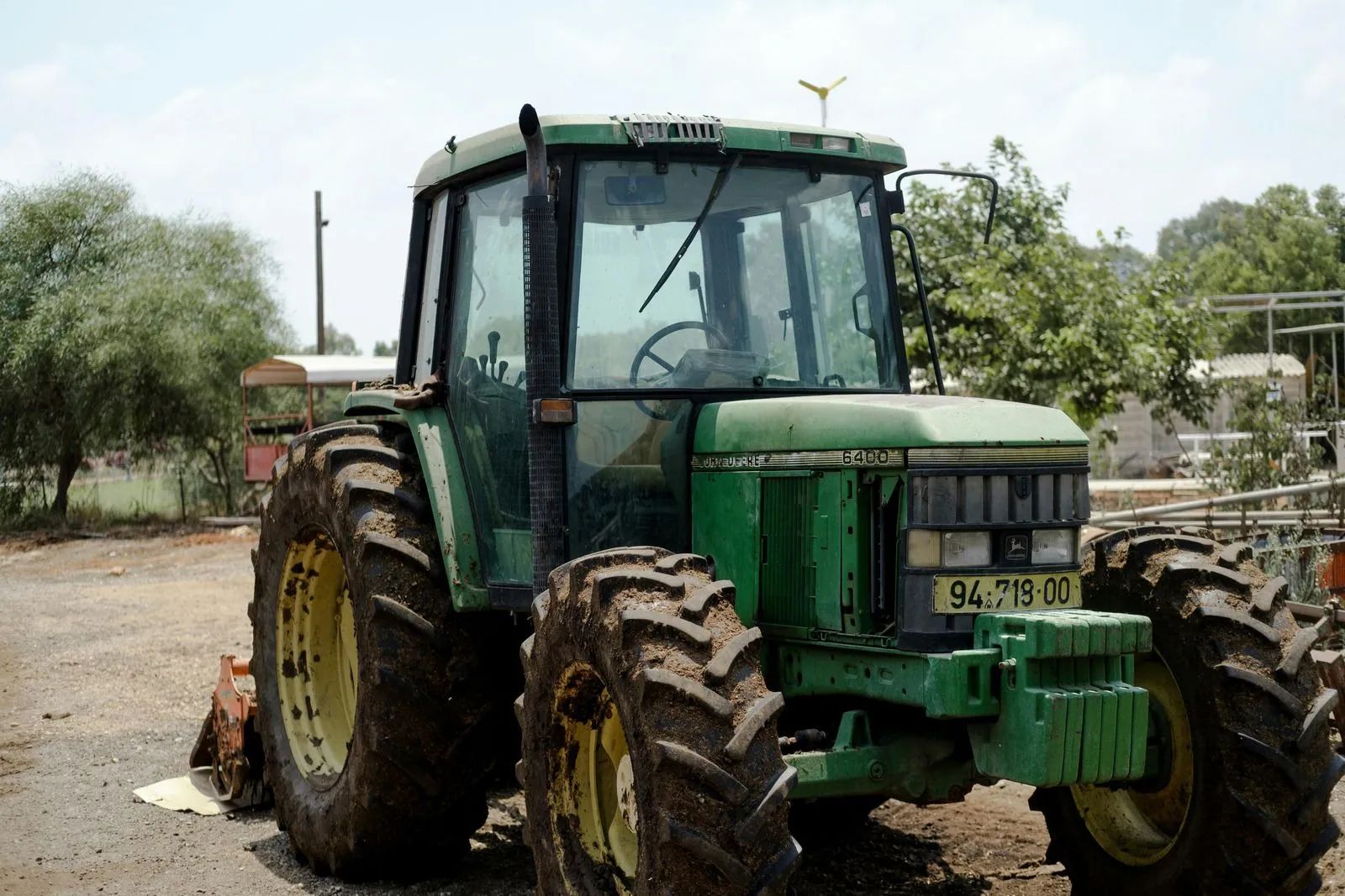 Green tractor parked on a dirt lot with trees in the background