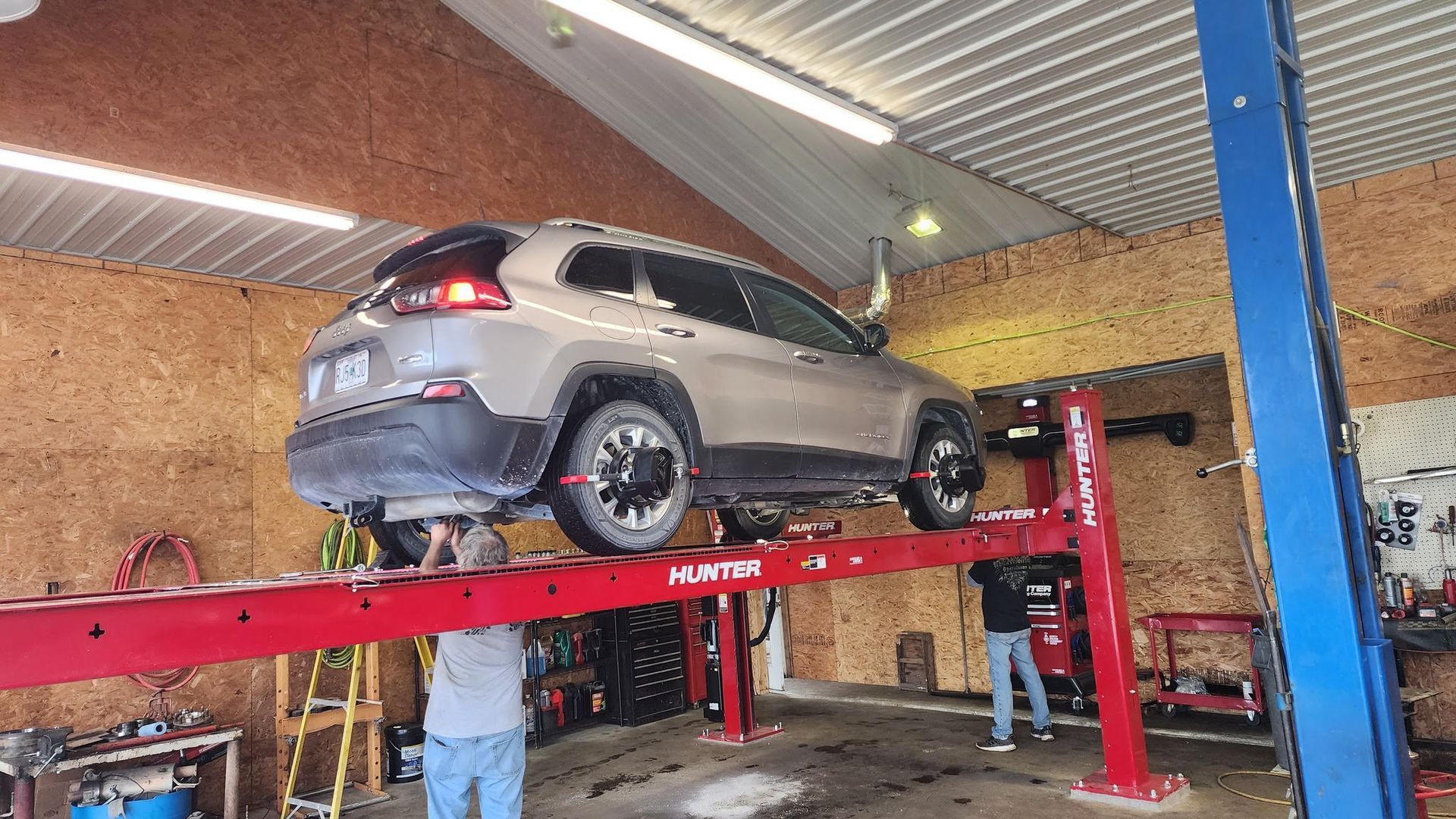 Tan SUV on a red car lift inside a garage, two people working below.