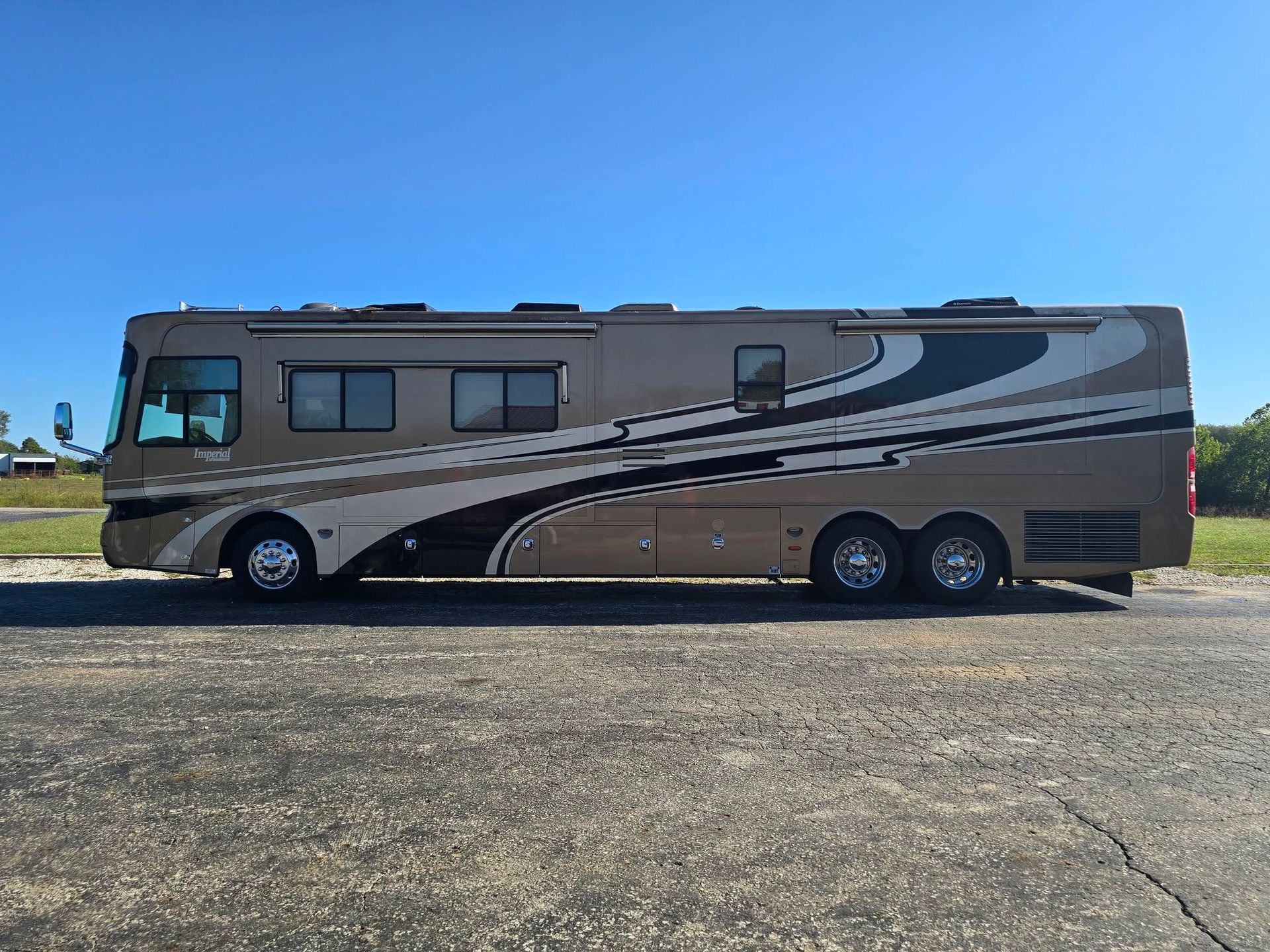Large tan and brown RV parked on an asphalt road under a clear blue sky.