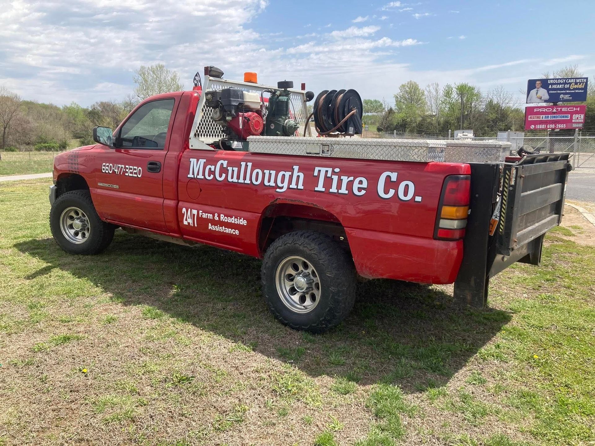 Red McCollough Tire Co. work truck parked on grass, tools in the bed, under a blue sky.