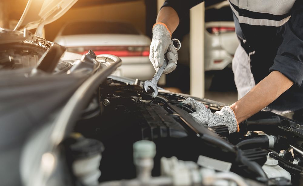 Mechanic in gloves, using a wrench to work on a car engine in a garage.