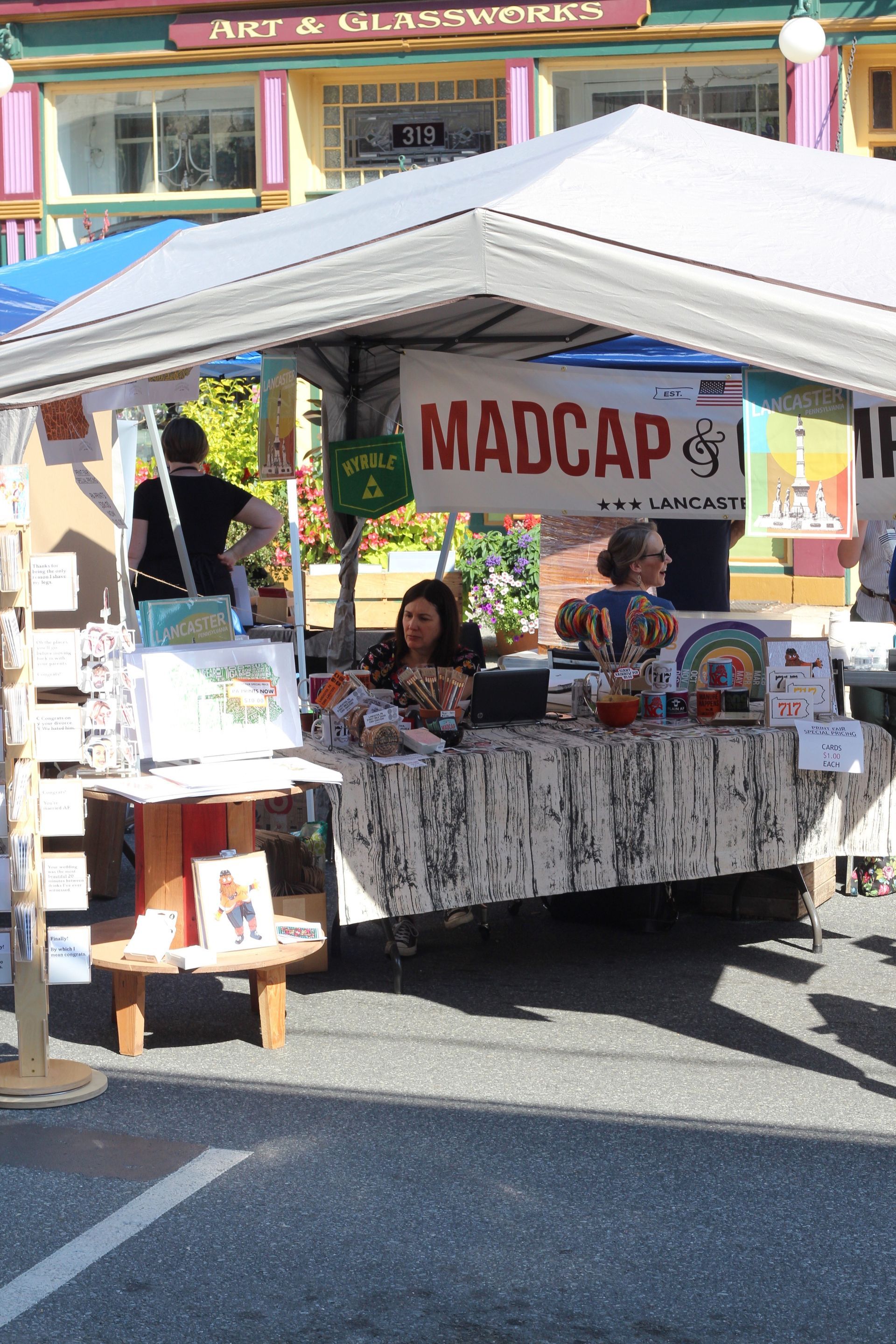 A woman is sitting at a table under a tent with a sign that says madcap.
