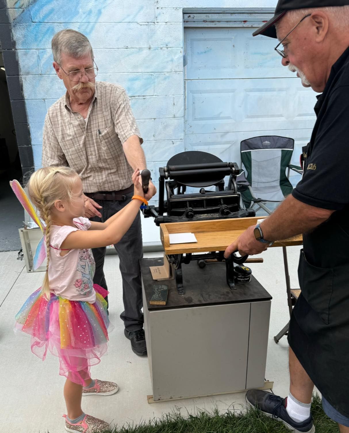 A little girl in a pink tutu is standing next to a man and a machine.