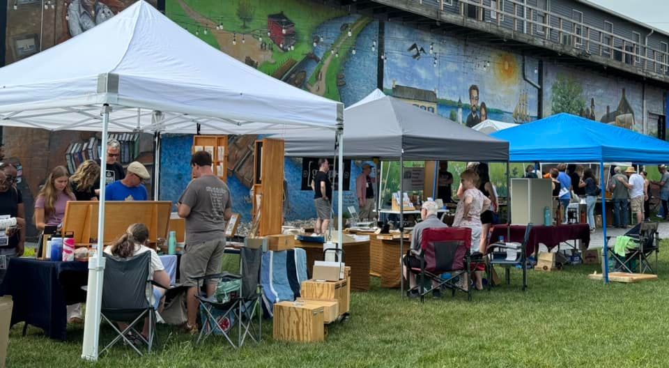 A group of people are sitting under tents in a field.