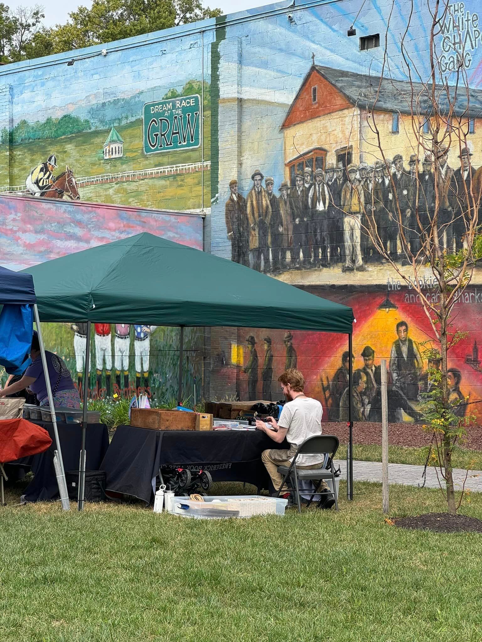 A man is sitting under a tent in front of a large mural.