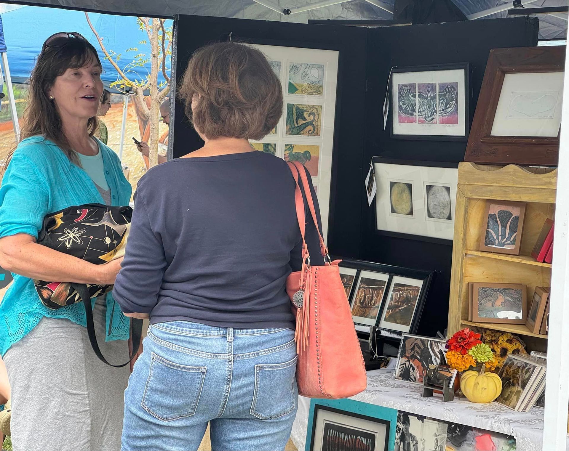 Two women are standing in front of a table with pictures on it.