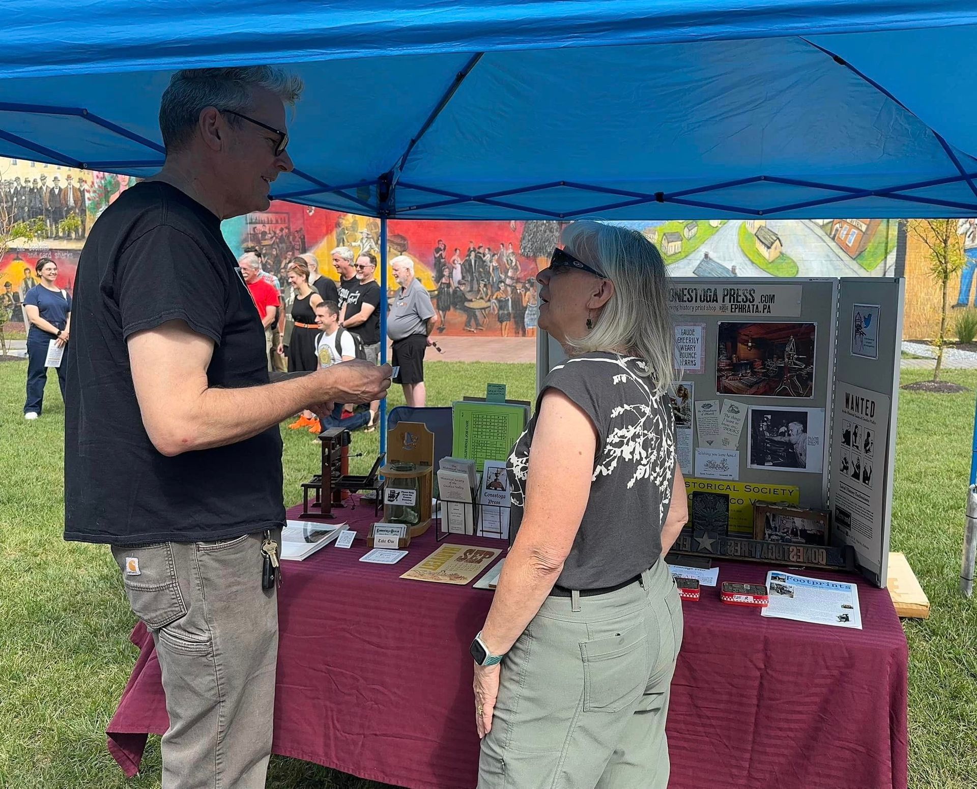 A man and a woman are standing under a blue tent talking to each other.
