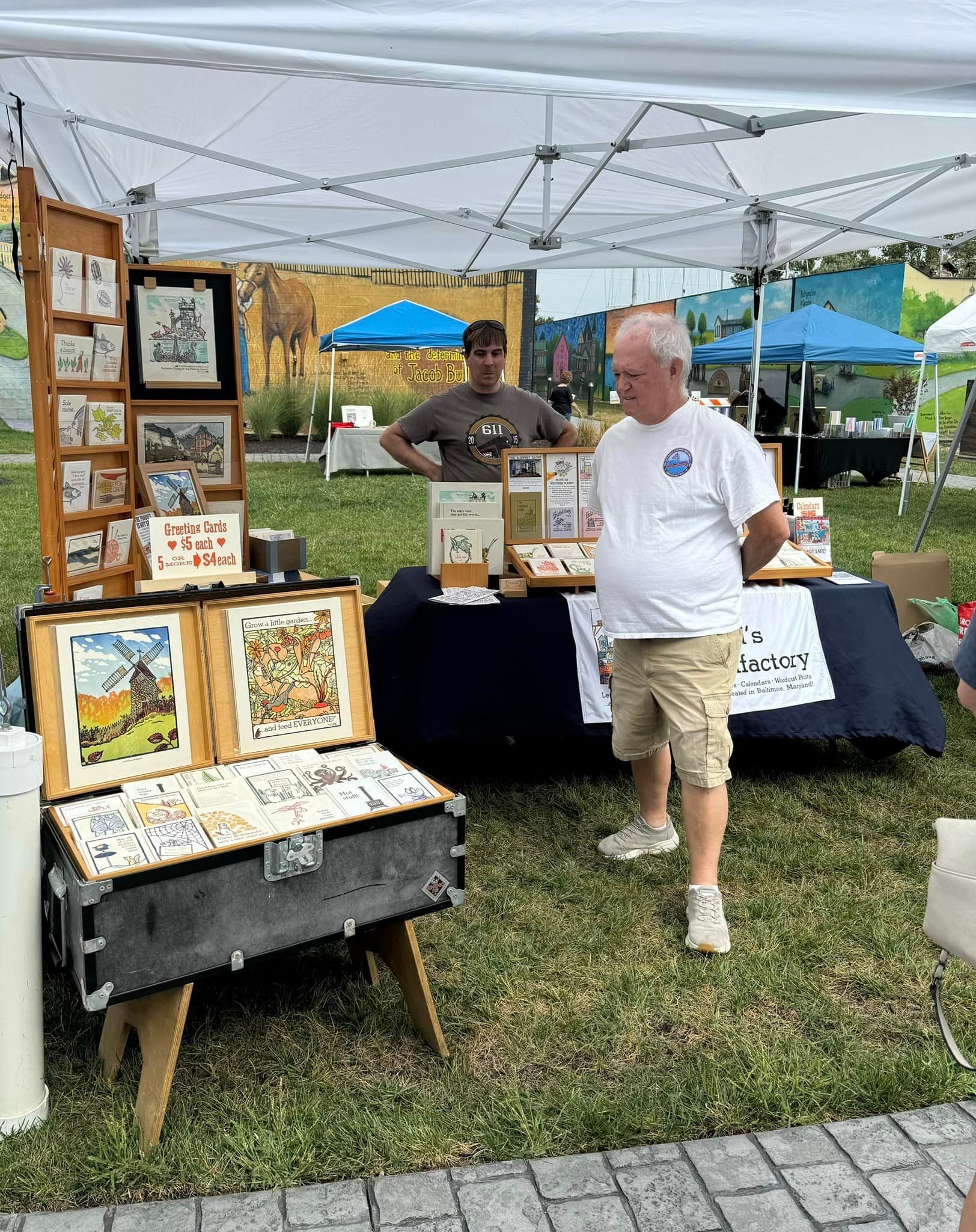 A man is standing in front of a table with paintings on it.