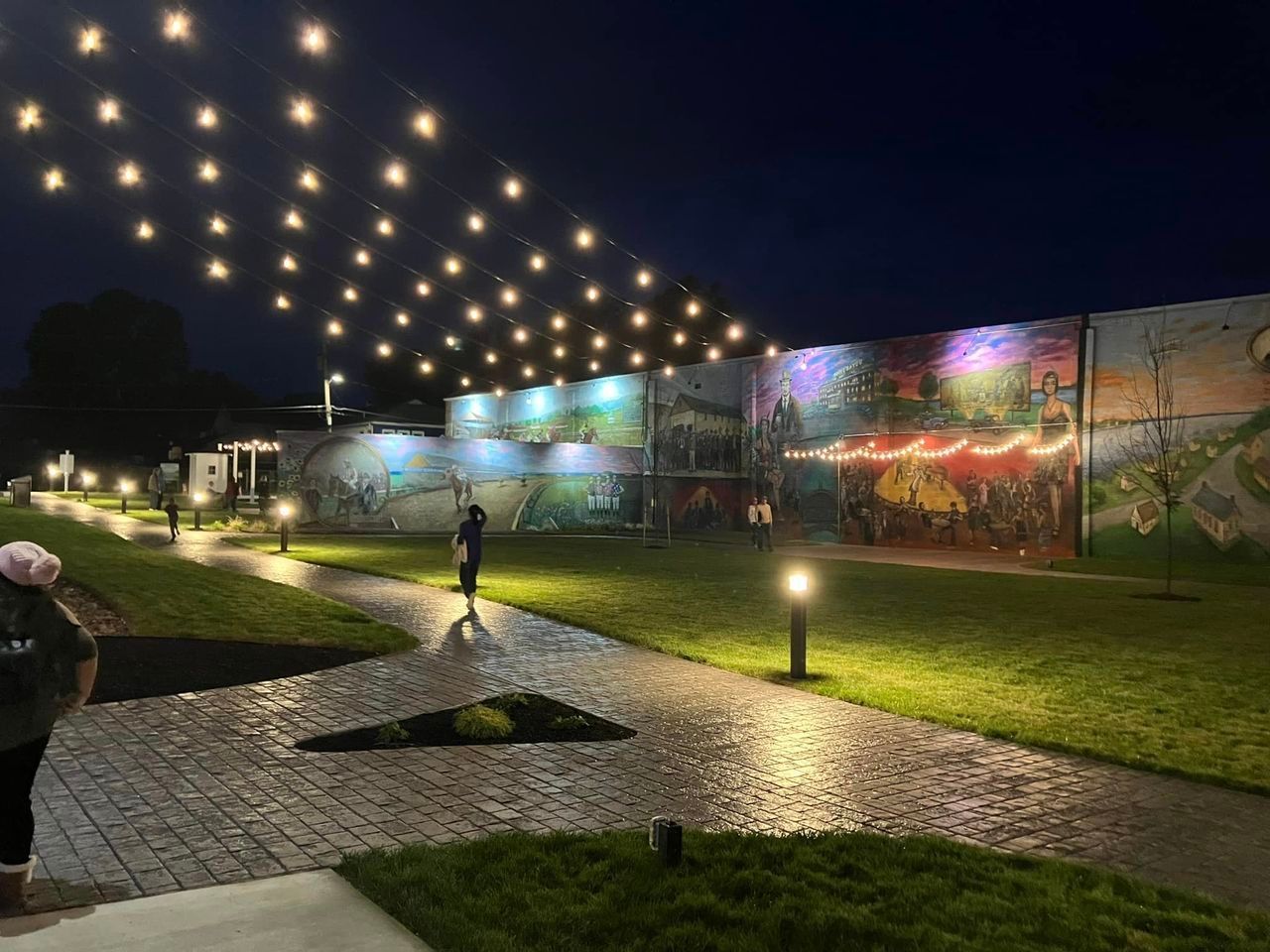 A person is walking down a sidewalk in a park at night.