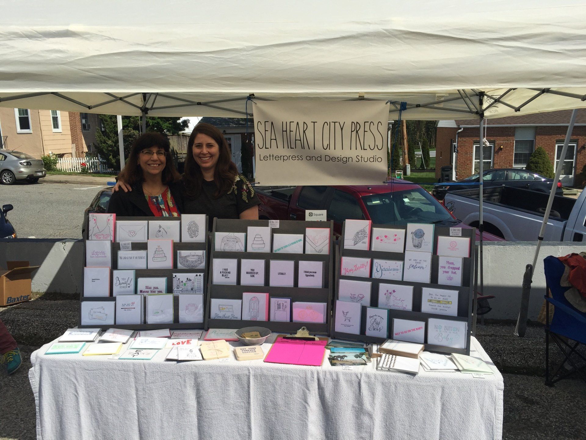 Two women are standing behind a table with cards on it under a tent.
