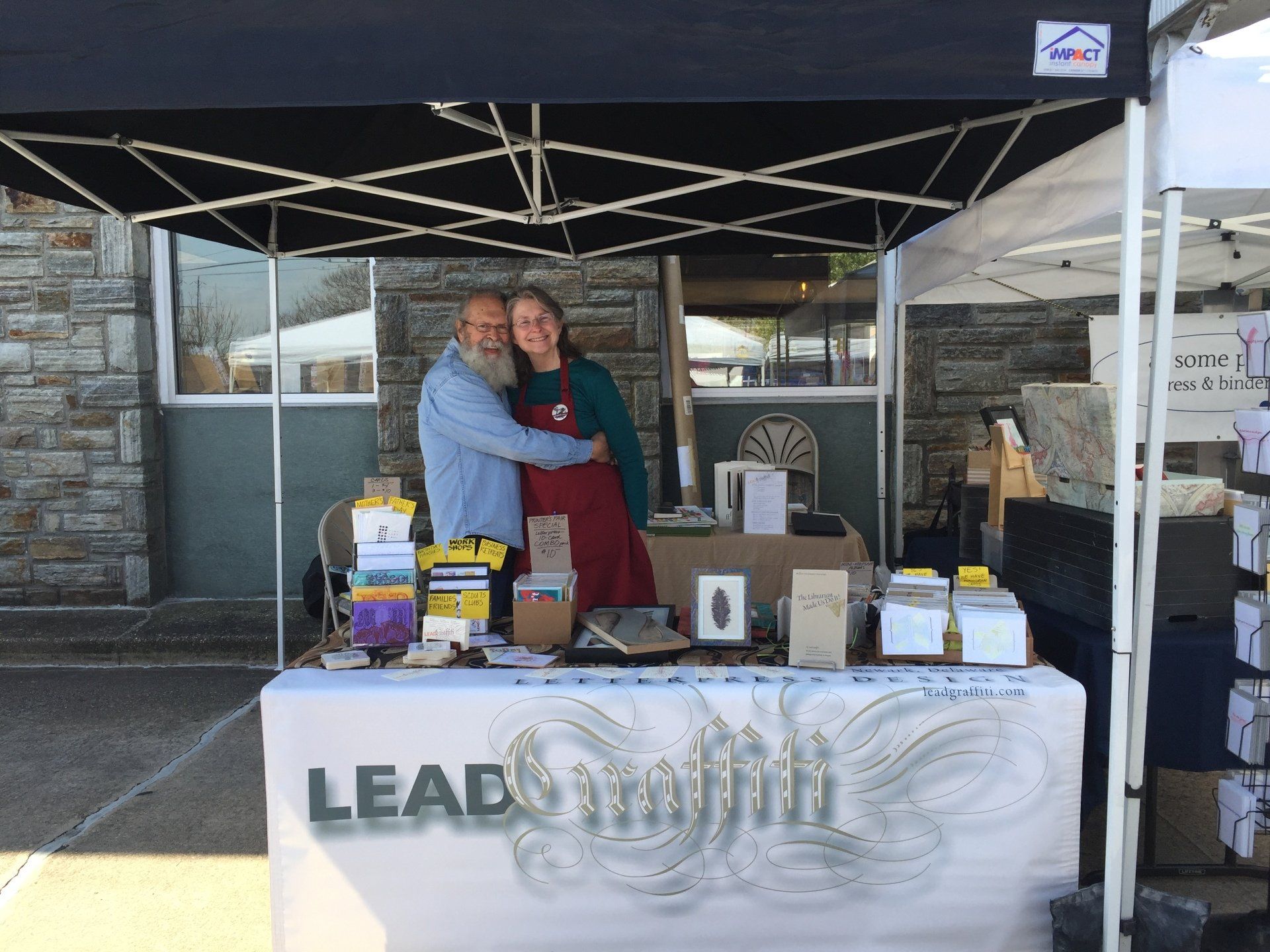 A man and a woman are standing behind a table under a tent.