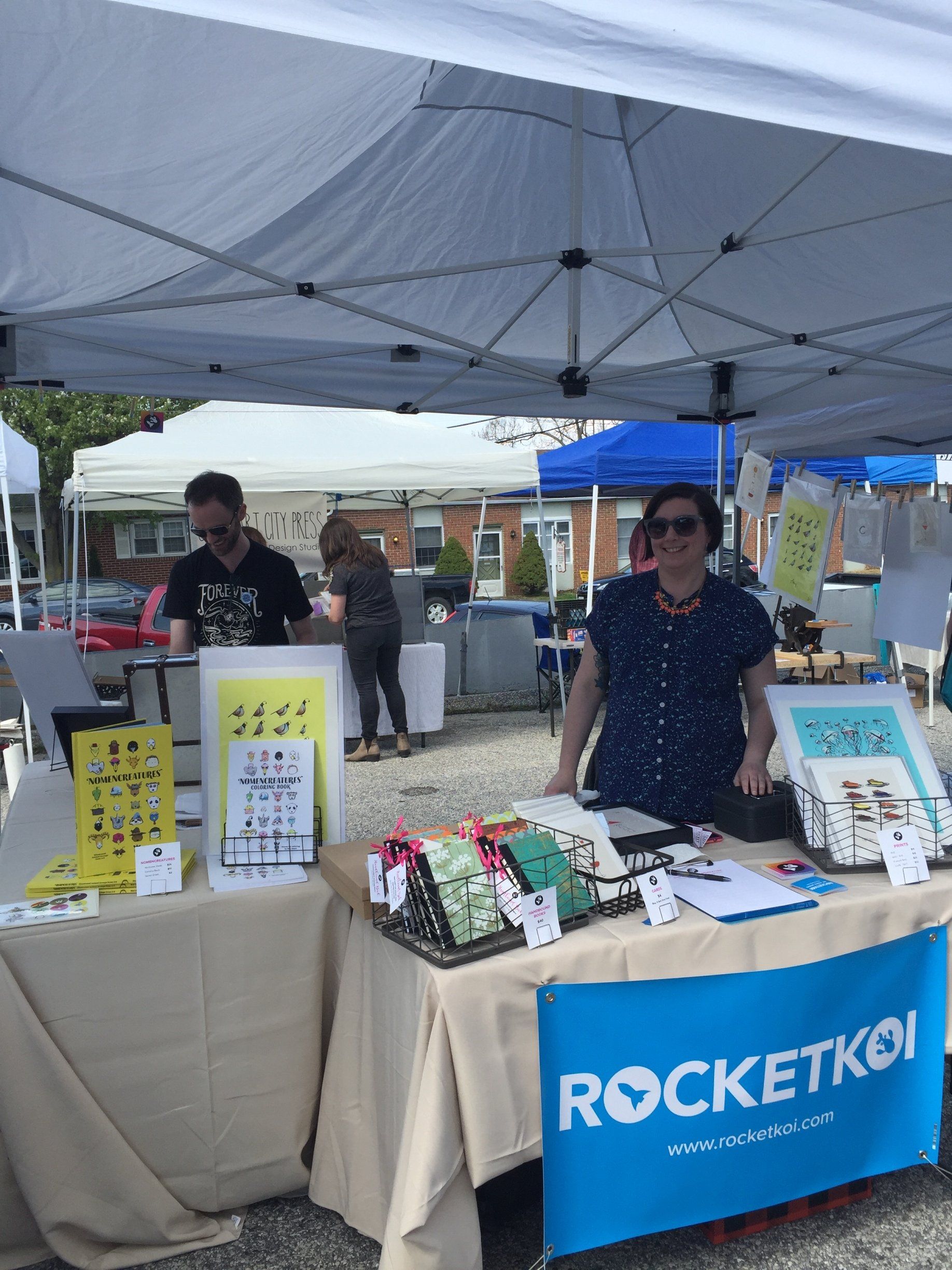 A woman stands behind a table with a sign that says rocketkot