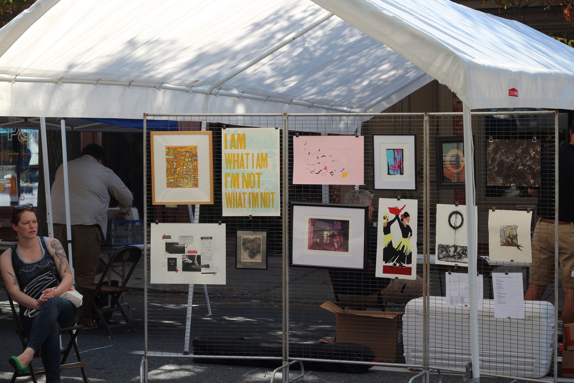 A woman sits under a tent with a sign that says 