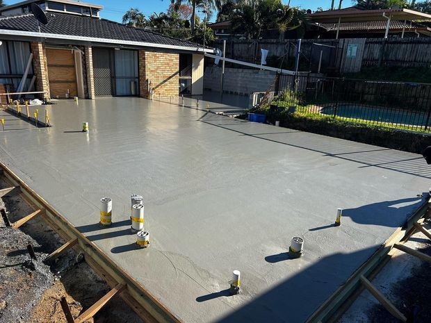 Fresh concrete slab being poured in a backyard construction site with house walls and pipes visible