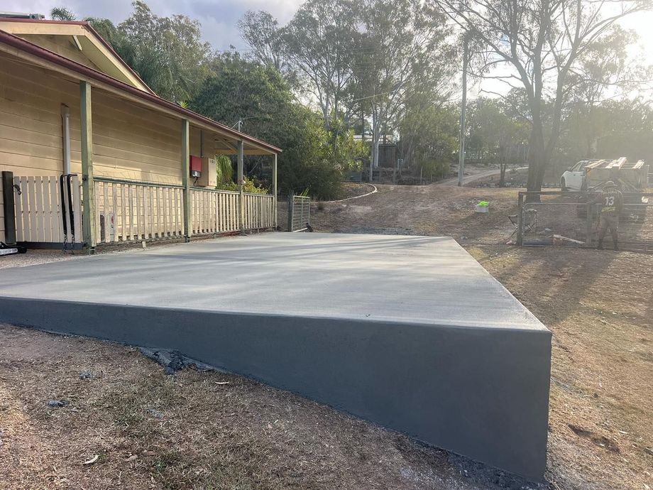 Concrete ramp beside a wooden building on a sloped dirt lot, leading up to a level platform