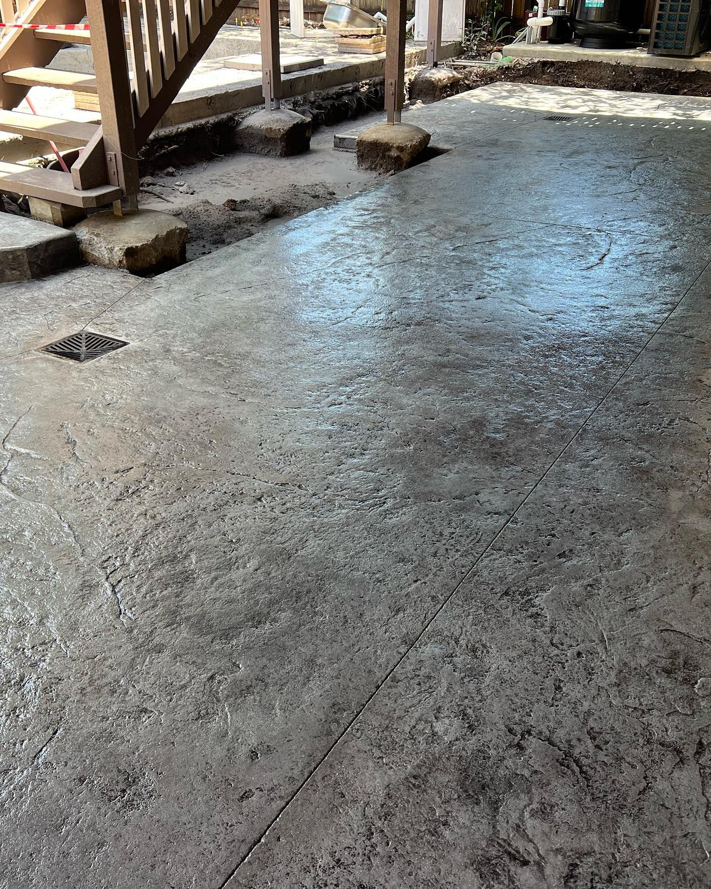 Freshly poured concrete slab under stairs with a small drain opening outdoors
