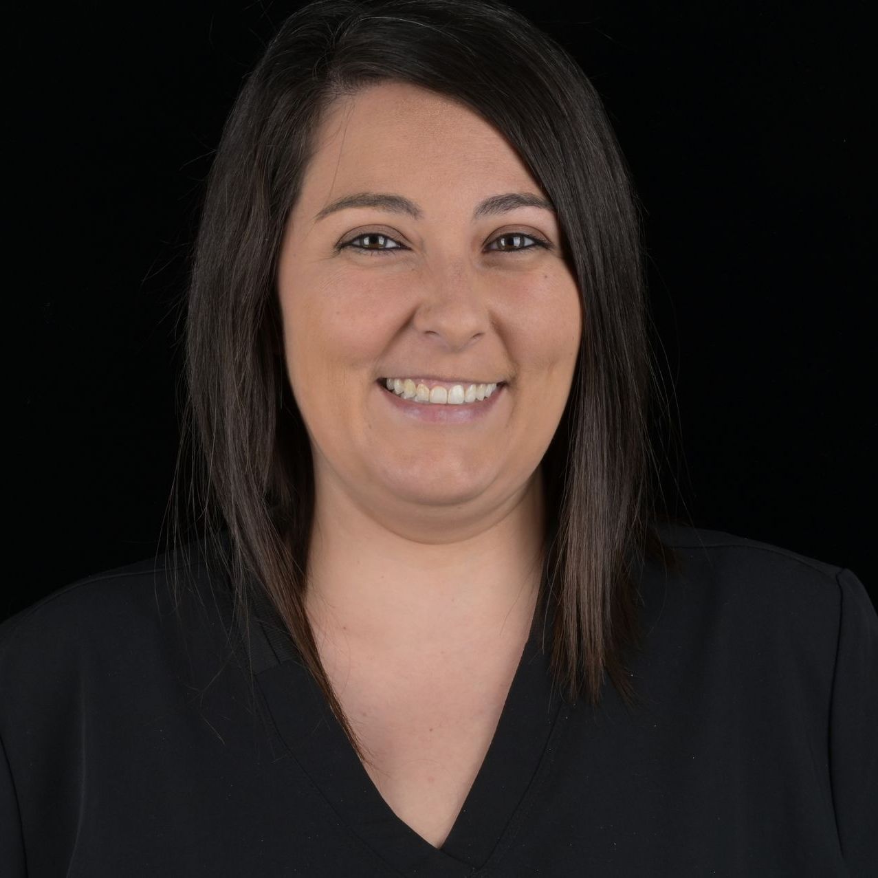 Woman with dark hair smiles, wearing a black top against a black background.