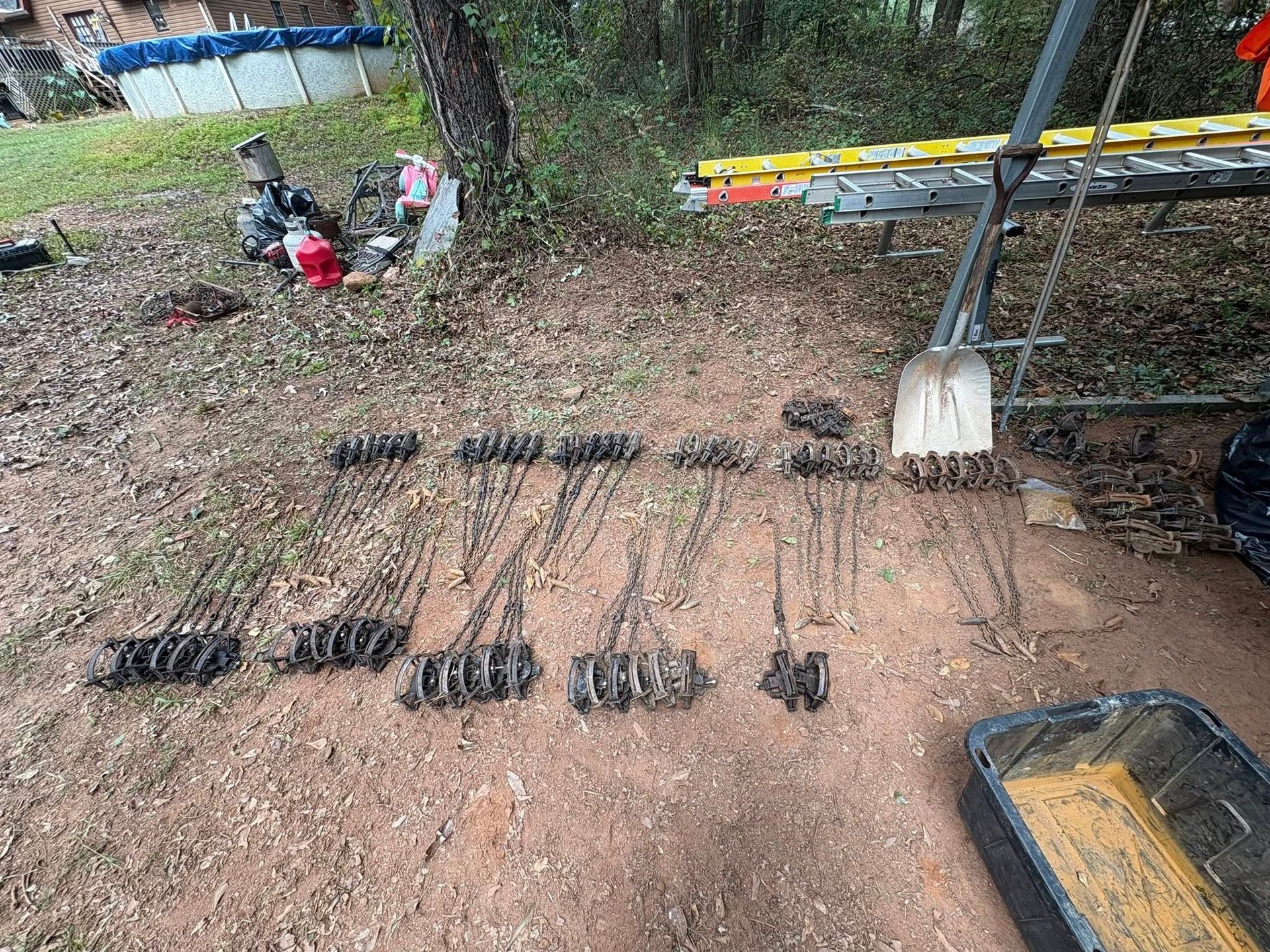 Metal animal traps laid out on the ground near a shovel and ladder.