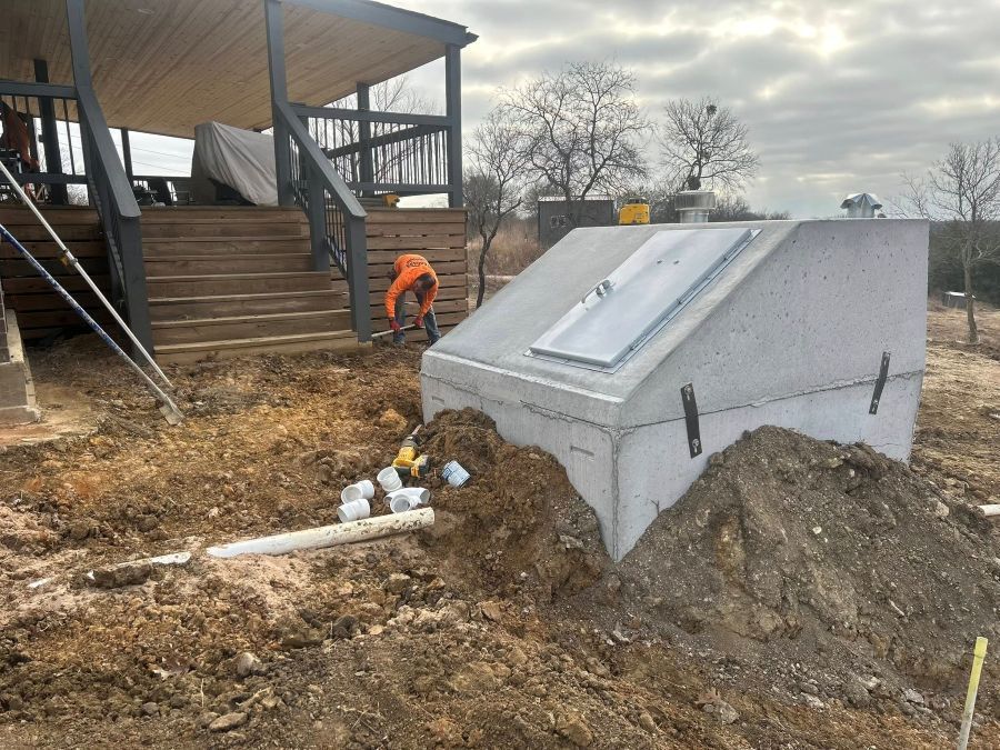 Concrete storm shelter being installed in front of porch steps  and worker in orange