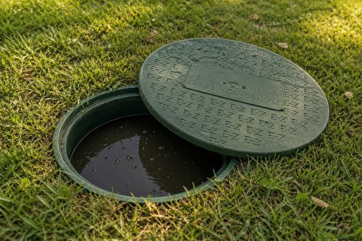 Open green utility cover beside a grassy lawn, with dark water visible inside the opening