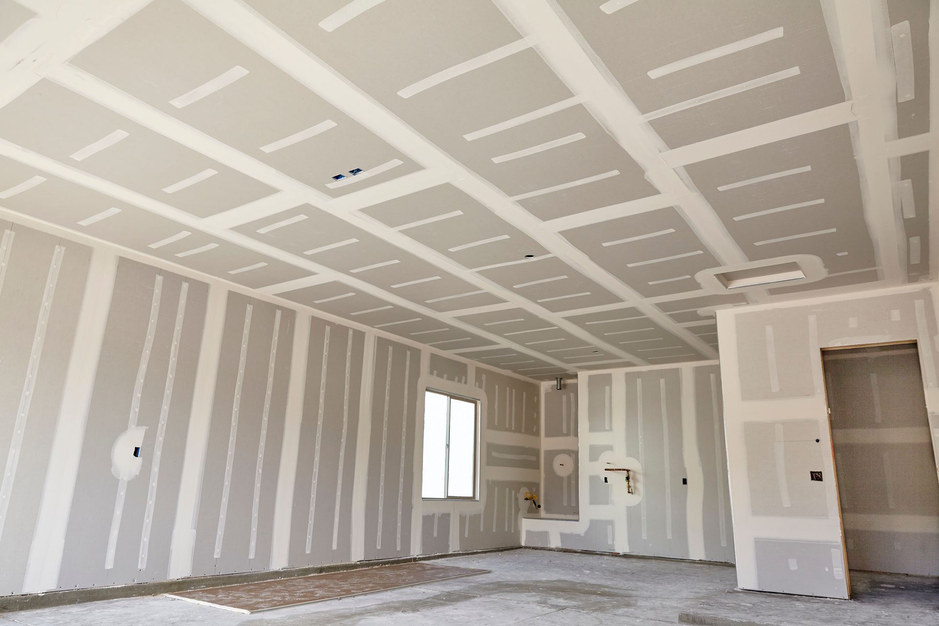 Interior view of a room with drywall installed on walls and ceiling, unfinished, with window and doorway.