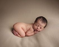 Newborn baby boy lying on his tummy on a beige blanket