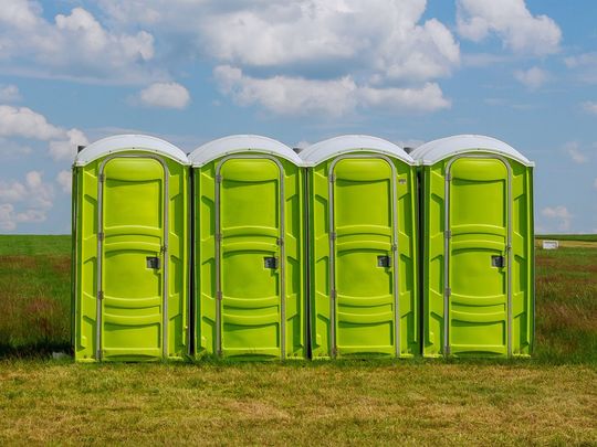 A row of green portable toilets are lined up in a field.