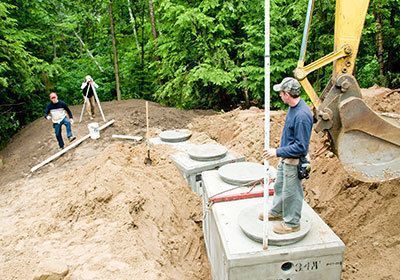 A man is standing next to a septic tank in the dirt.