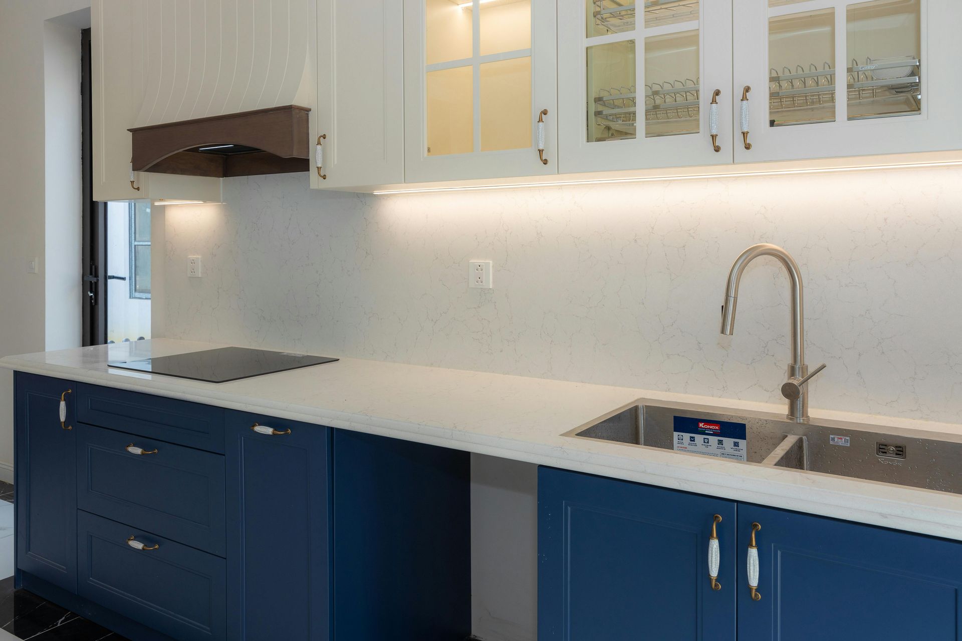 Modern kitchen with white cabinets, navy lower cabinets, white countertop, and stainless steel sink and stove.