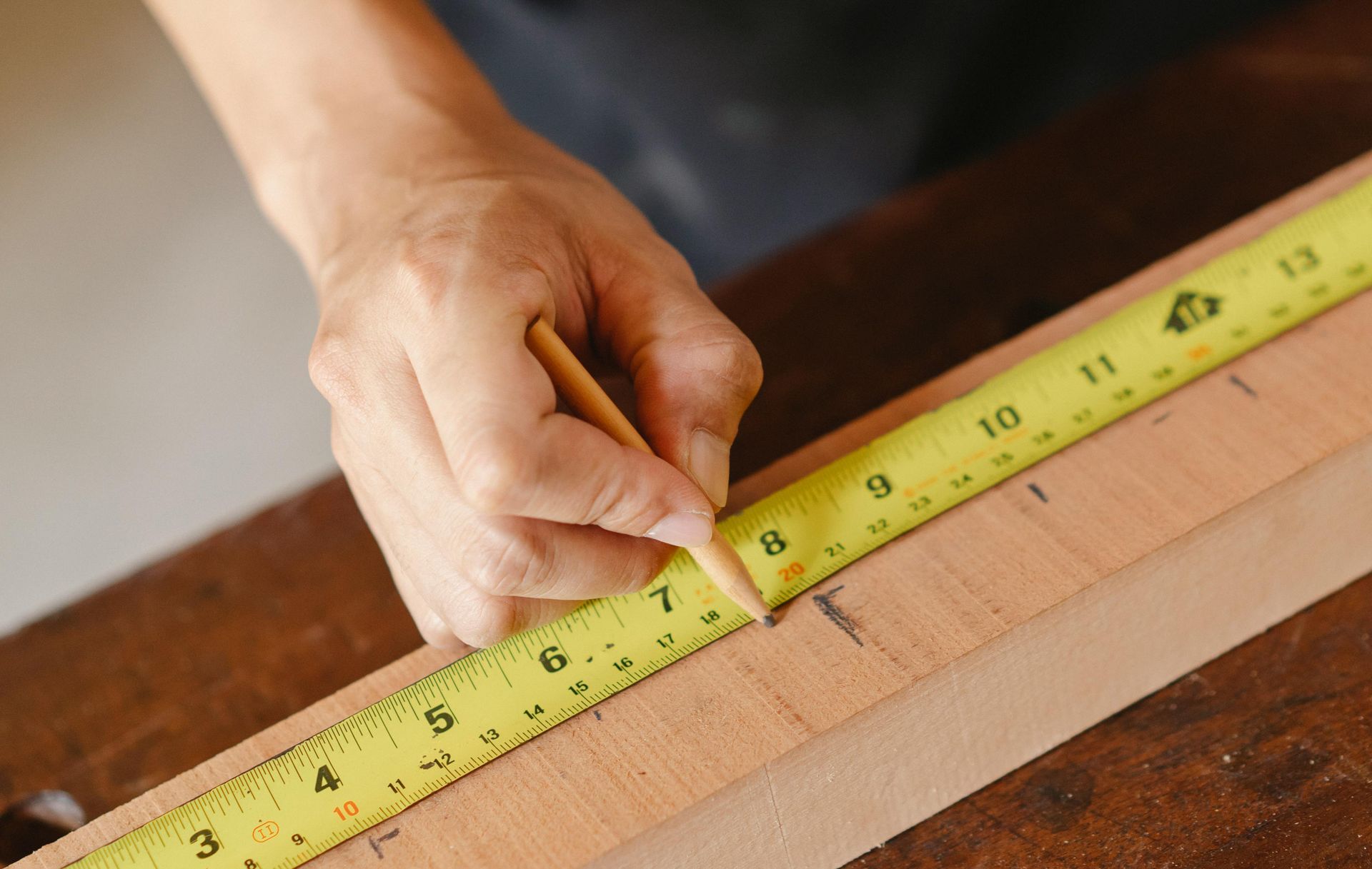 Hand measuring a wooden board with a yellow tape measure on a workbench