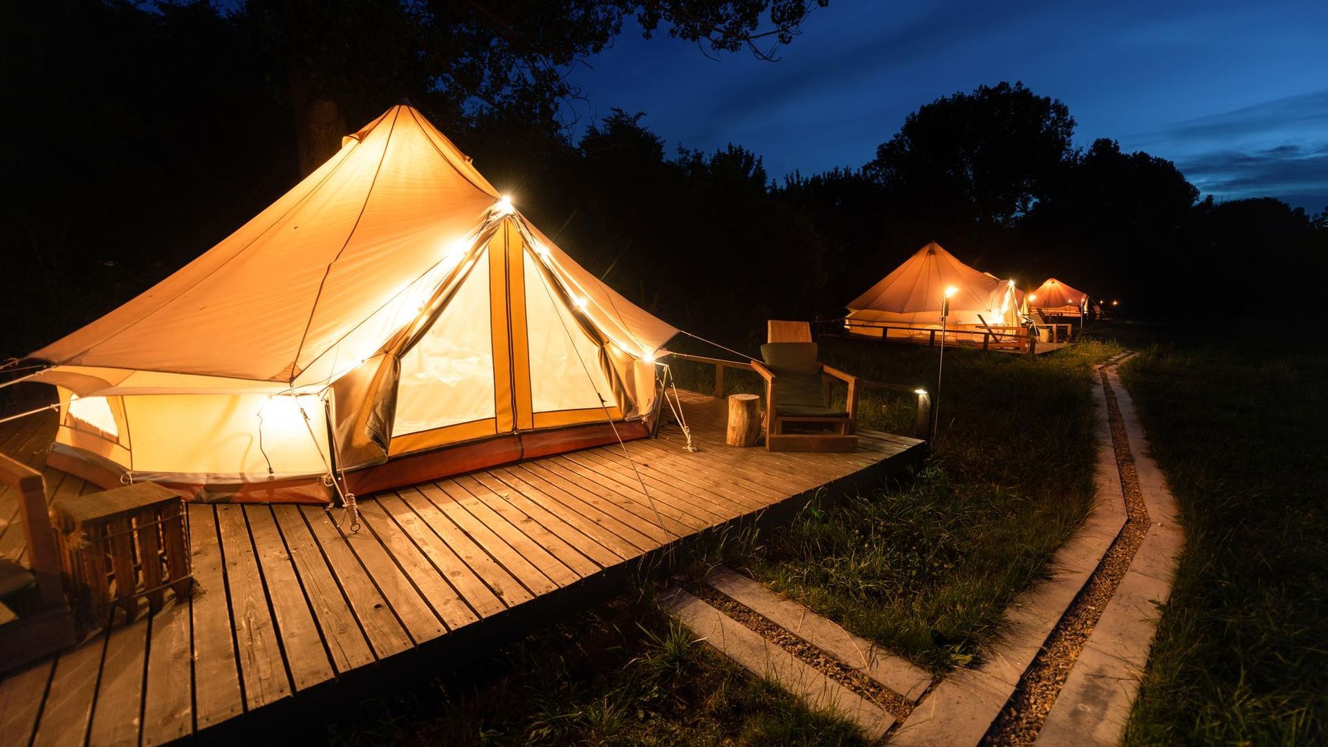 A tent is lit up at night on a wooden deck