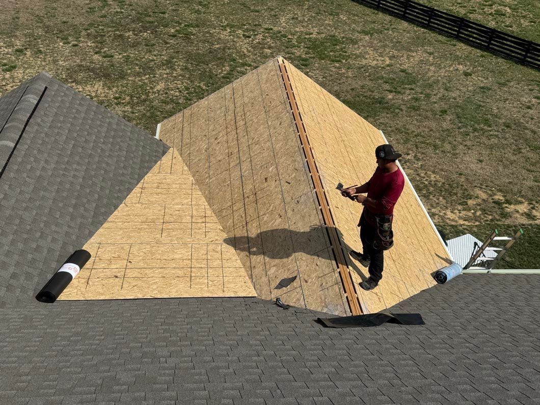 A man is standing on top of a roof holding a piece of plywood.