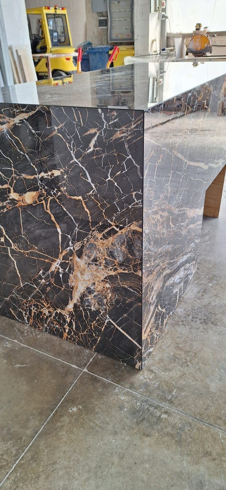 un ripiano in marmo nero e oro in una cucina con un carrello elevatore giallo sullo sfondo.