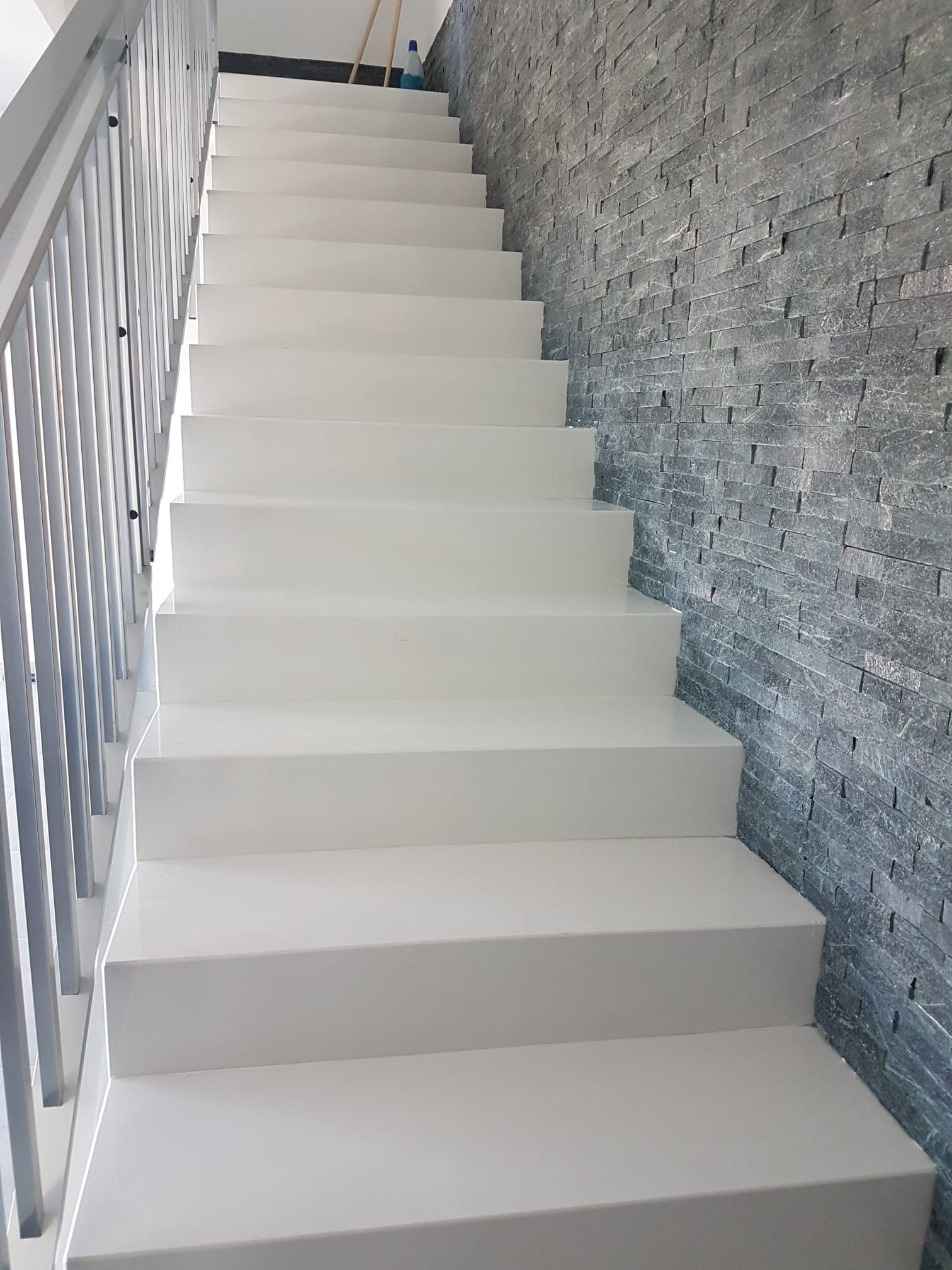 una serie di scale bianche con ringhiera in metallo che conducono a un muro di pietra.