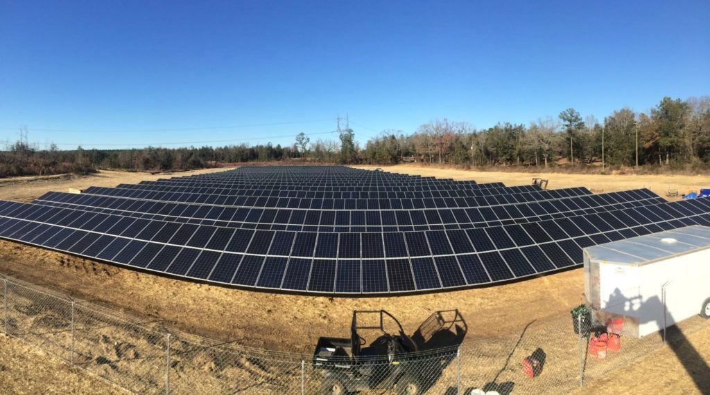 A large amount of solar panels are sitting on top of a dirt field.