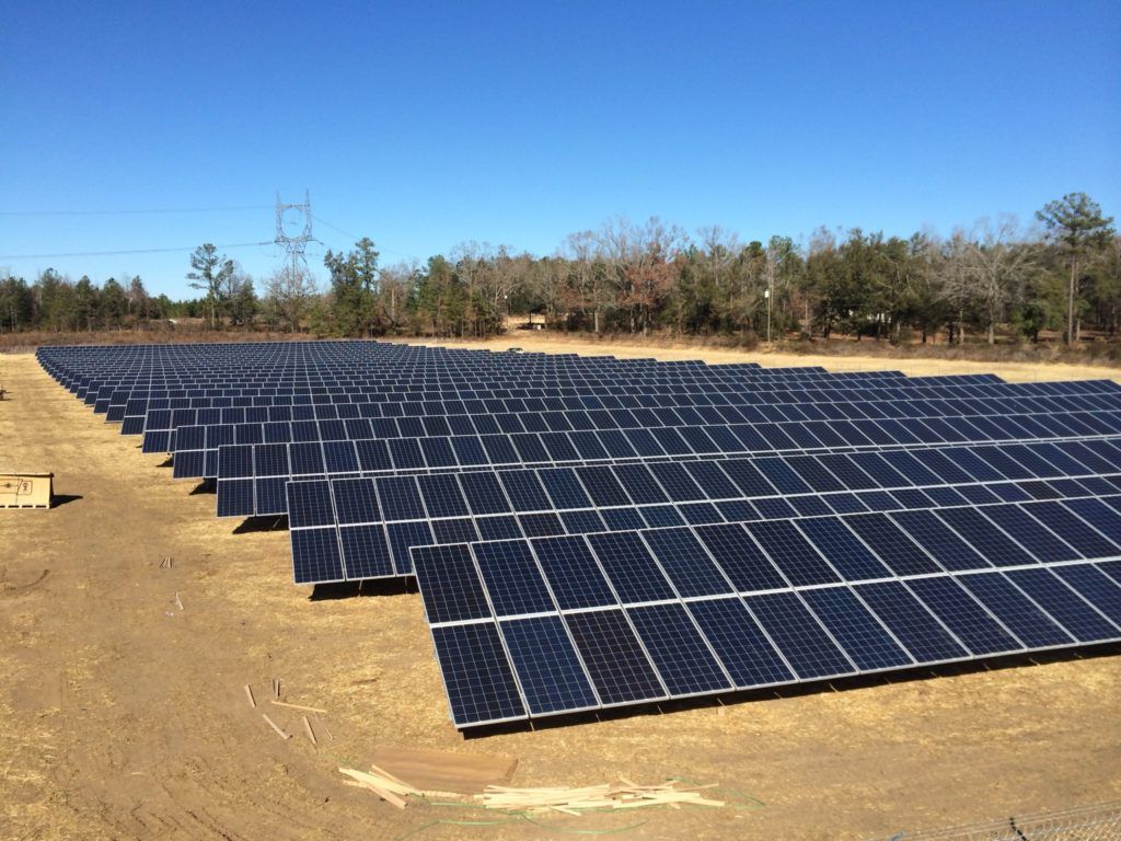 A large field of solar panels sitting on top of a dirt field.