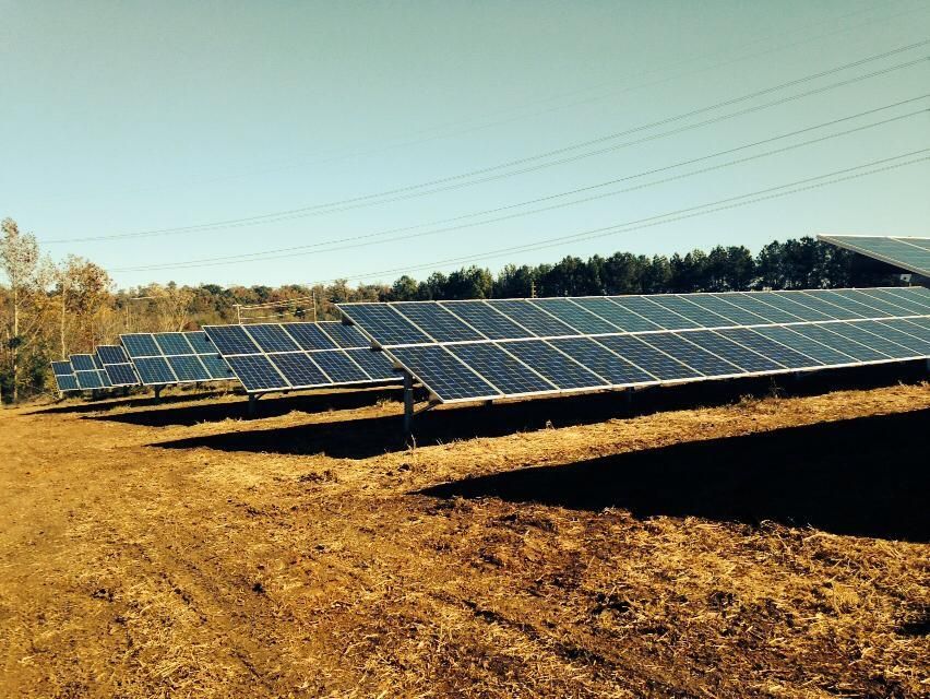 A row of solar panels sitting on top of a dirt field.